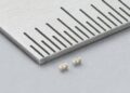 Two Murata LLD three-terminal MLCCs beside a metal ruler, showing beige ceramic bodies and silver-coloured terminals.