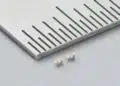 Two Murata LLD three-terminal MLCCs beside a metal ruler, showing beige ceramic bodies and silver-coloured terminals.