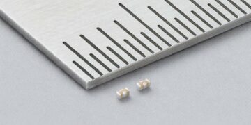 Two Murata LLD three-terminal MLCCs beside a metal ruler, showing beige ceramic bodies and silver-coloured terminals.
