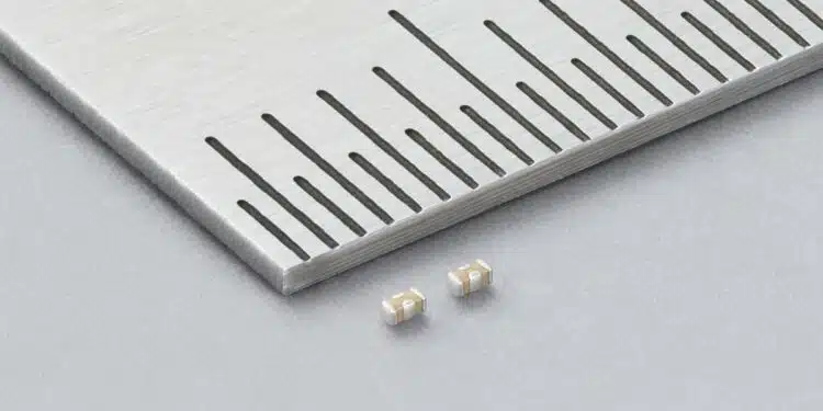 Two Murata LLD three-terminal MLCCs beside a metal ruler, showing beige ceramic bodies and silver-coloured terminals.